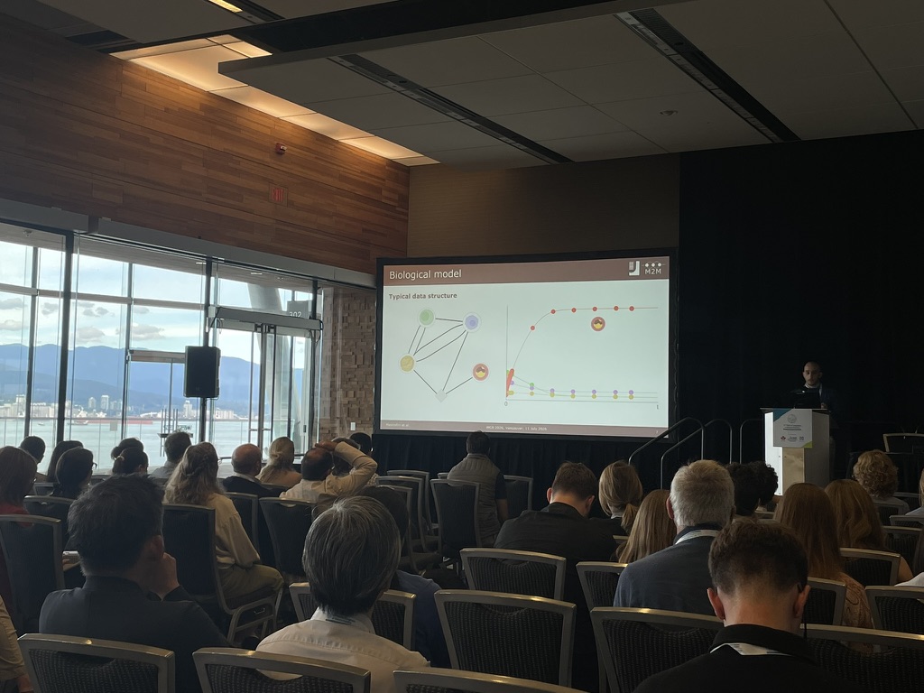 A scientific presentation at the Vancouver congress, with a biological model slide and the harbour visible through the windows.